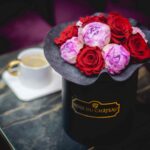 Rose du Chateau opinie czy warto bukiet wiecznych róż i piwonii w czarnym pudełku na tle stolika kawowego, na którym stoi kawa. Flowerbox widoczny nieco od góry