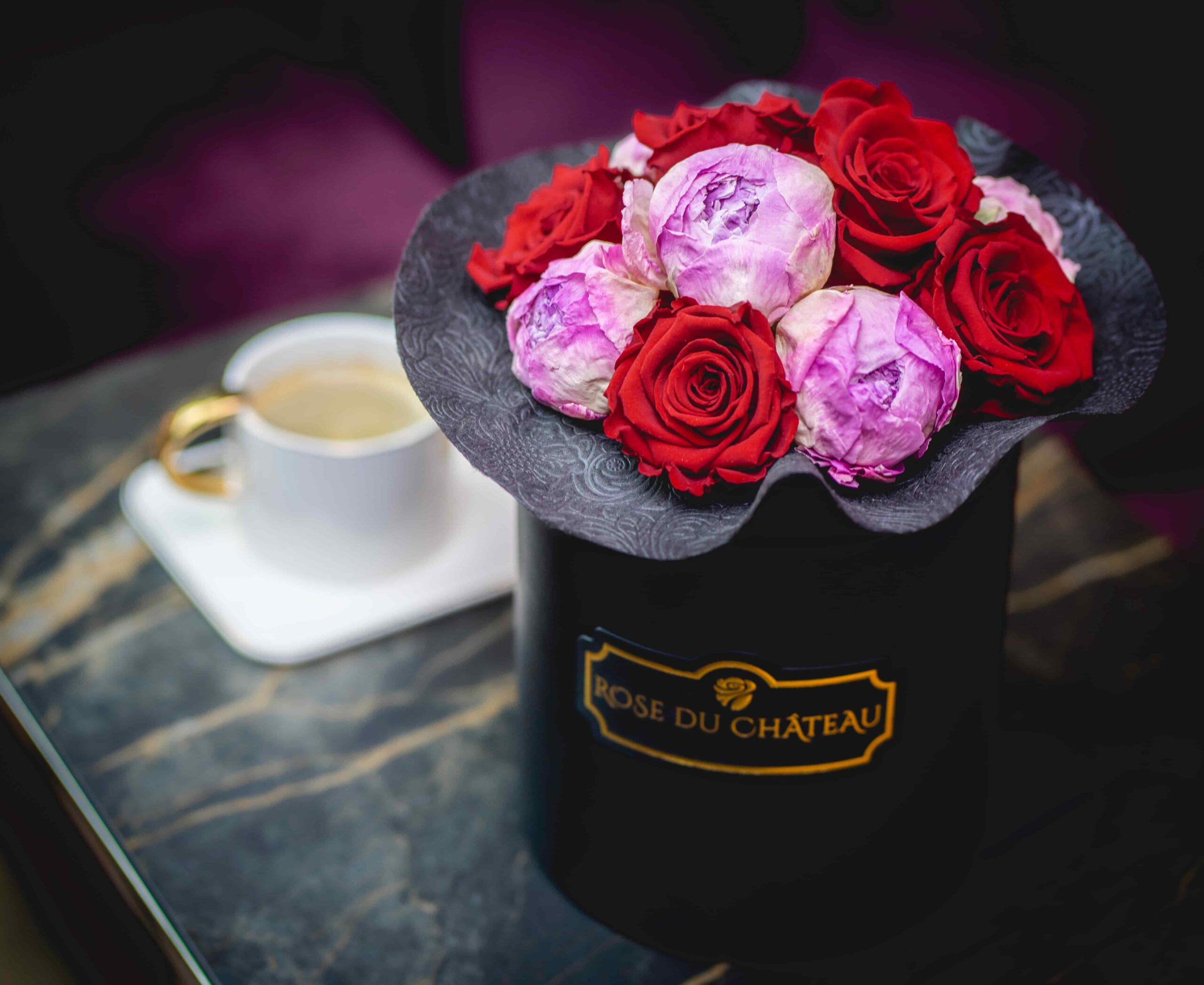 Rose du Chateau opinie czy warto bukiet wiecznych róż i piwonii w czarnym pudełku na tle stolika kawowego, na którym stoi kawa. Flowerbox widoczny nieco od góry